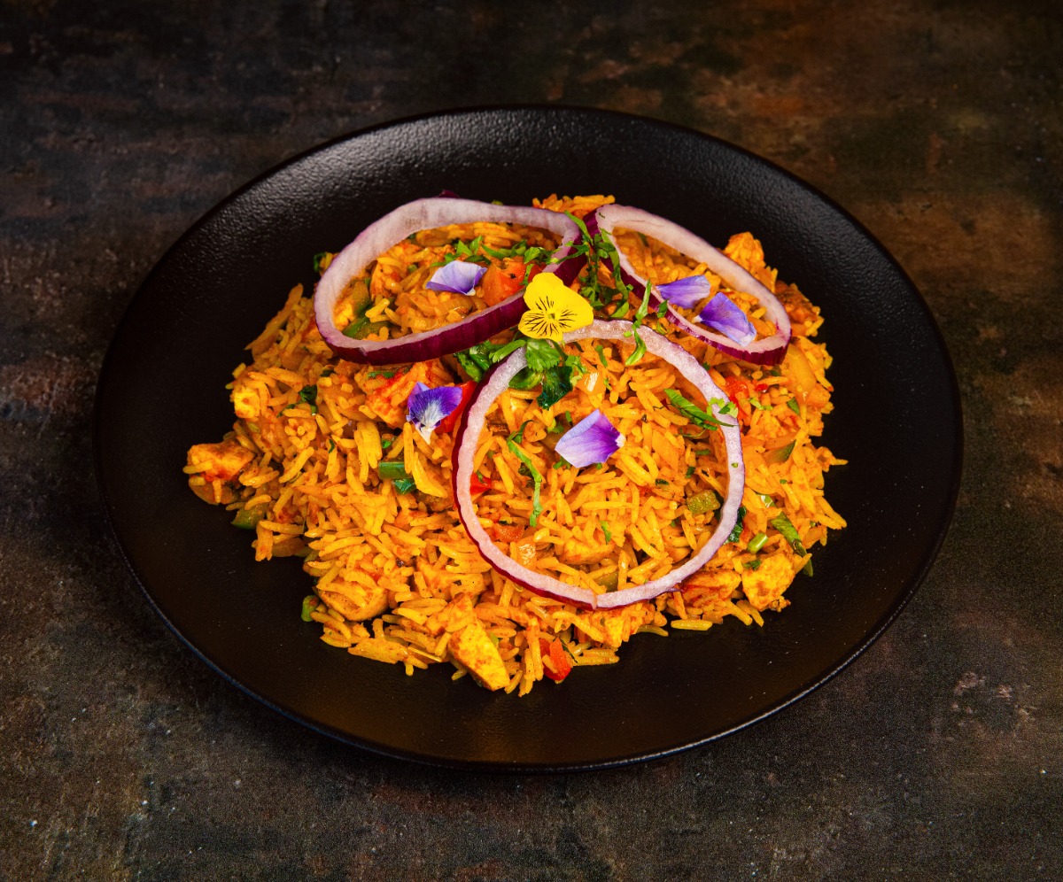 Enjoy delicious Indian curry from Thindian in Leyland Rice dish on a dark place garnished with ring of onion and flower petals f