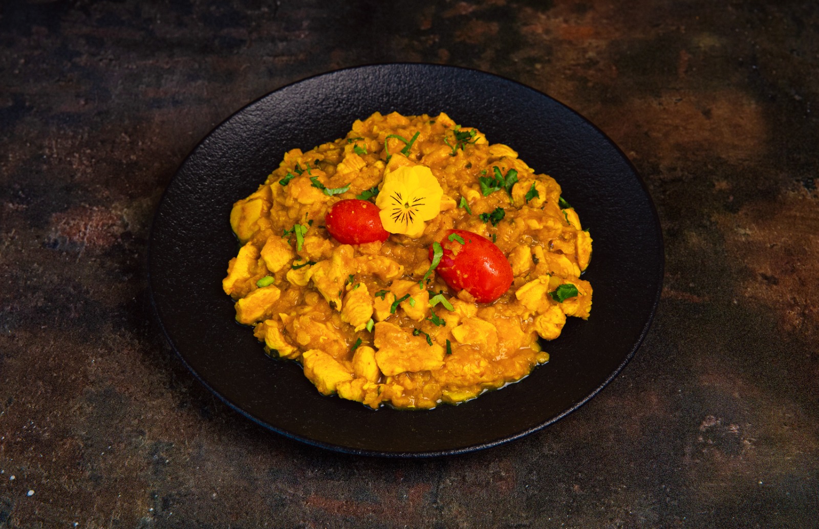 Authentic Indian food ready for takeaway in Leyland Dark plate with vibrantly coloured chicken curry garnished with herbs and a pansy